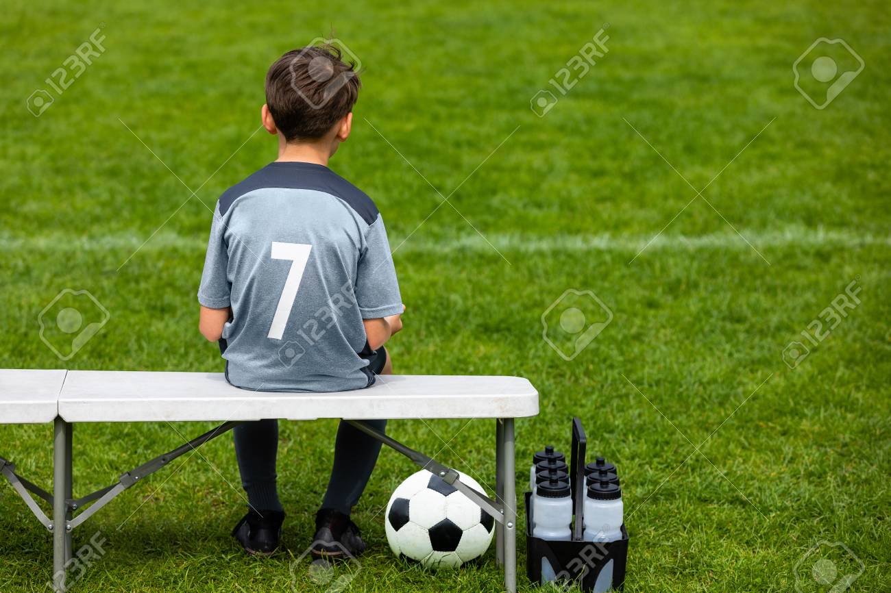 101121026-little-footballer-sitting-on-a-wooden-bench-and-watching-soccer-game-young-substitute-player